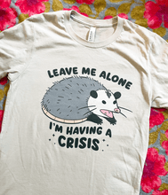 Load image into Gallery viewer, Beige t-shirt with an opossum graphic and text &#39;Leave me alone I&#39;m having a crisis&#39; on a floral background
