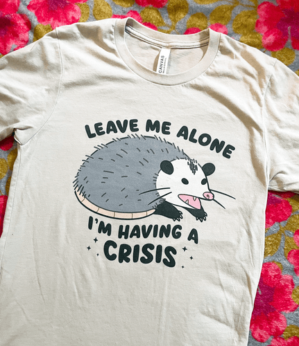 Beige t-shirt with an opossum graphic and text 'Leave me alone I'm having a crisis' on a floral background